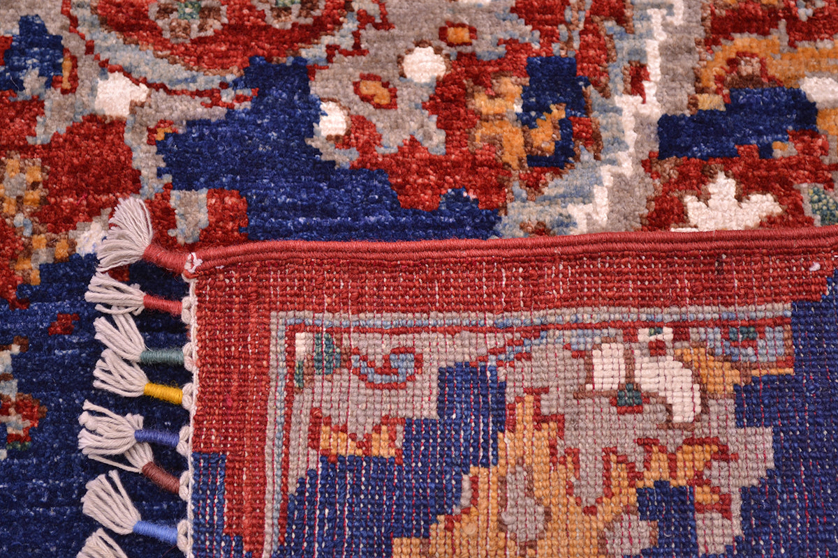 Close-up of the knotted back of a Handmade Modern Sickle-Leaf carpet patterned area rug corner showing a red border, cream and blue field, and white tassels.