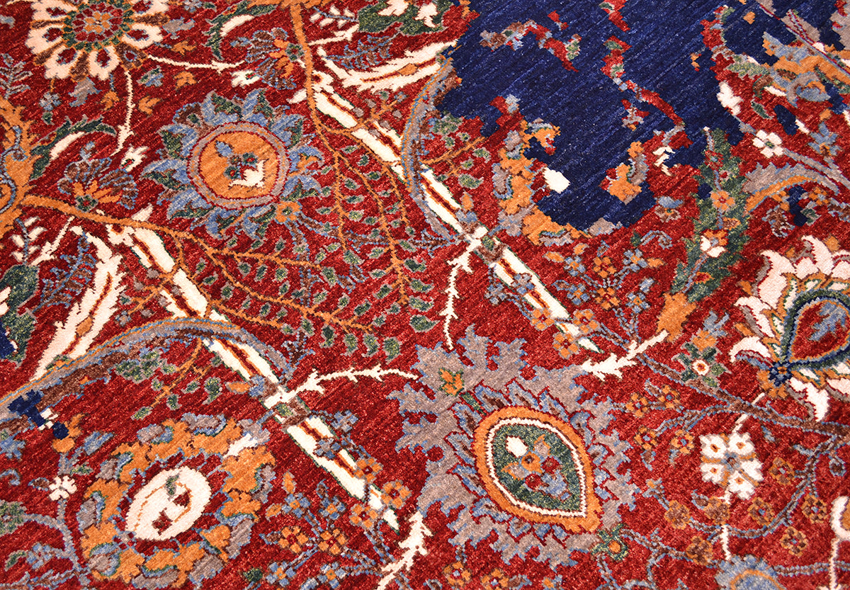 A close-up of a handmade Modern Sickle-Leaf carpet with a deep red field, featuring cream, blue, orange, and green floral and paisley motifs.
