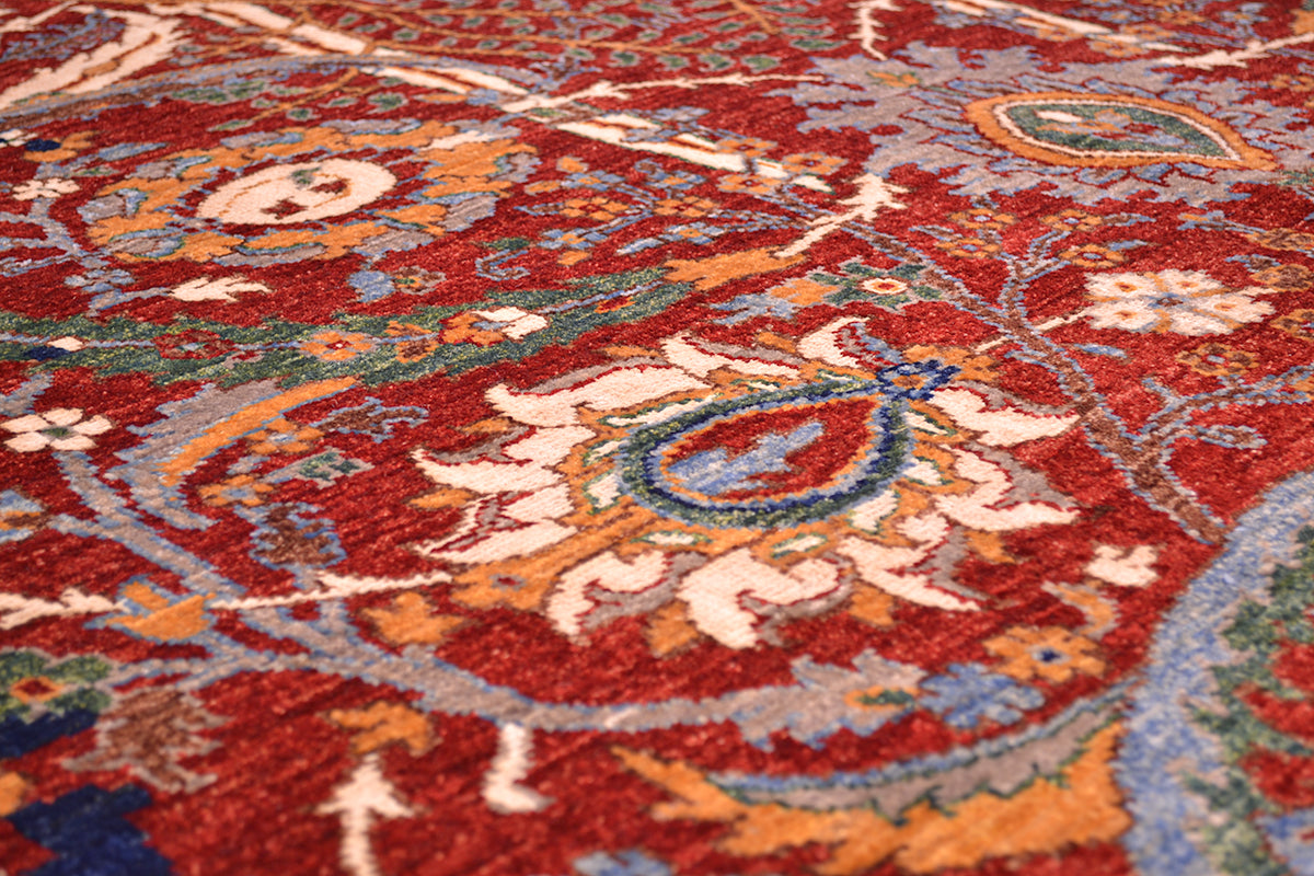 A close-up of a traditional patterned rug with a deep red field, featuring cream, orange, blue, and green floral and paisley motifs.