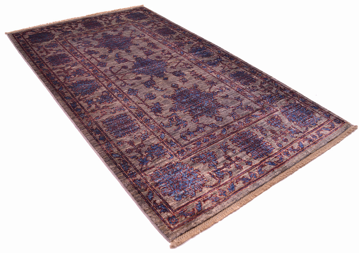 Angled view of handmade Afghan Rug ith pewter grey field colour and all over flroal design woven on a cotton foundations with latticed fringes. Blue floral motifs with deep chesnut red outlining.