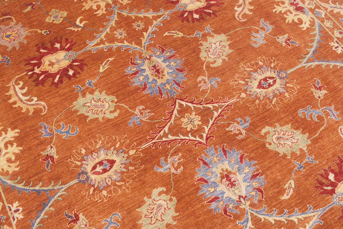 Detailed view of handknotted carpet with warming cinnamon/ amber toned main field with spacious floral motifs in red, blue, soft light green and cream.