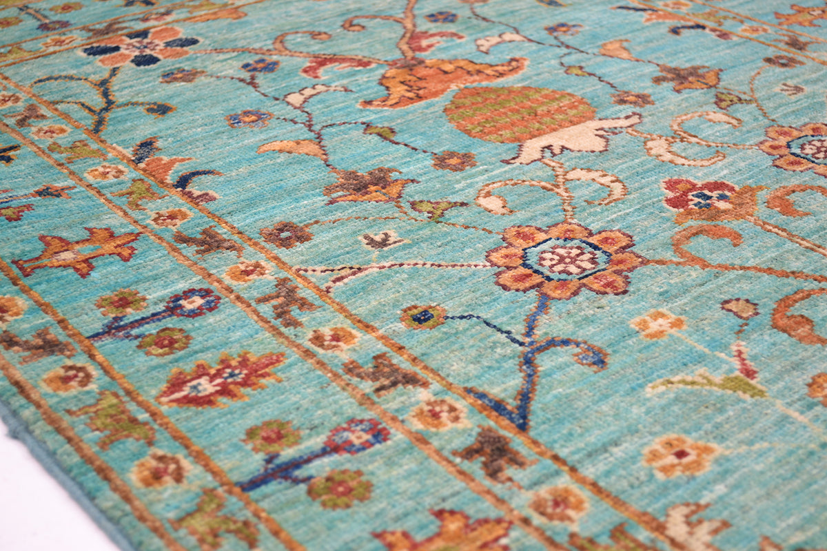 Detail of stylized floral border and minor borders of handmade rug with light turquoise. blue, orange, reds and leafy greens.