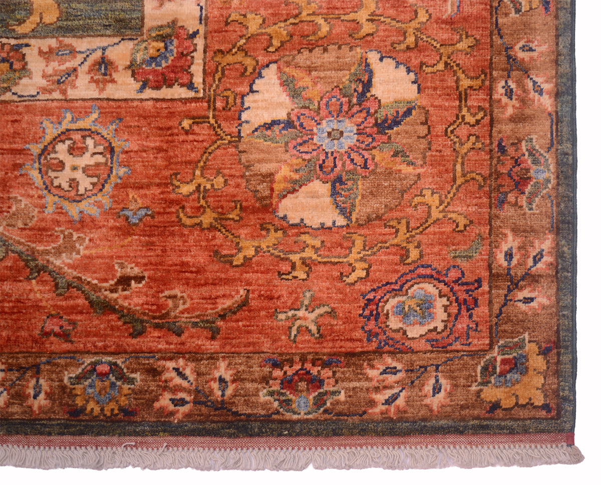 A close-up of an Afghan Suzani design handmade carpet corner showing a warm rust-red field with floral medallions, beige and blue accents, and a dark border with fringe.