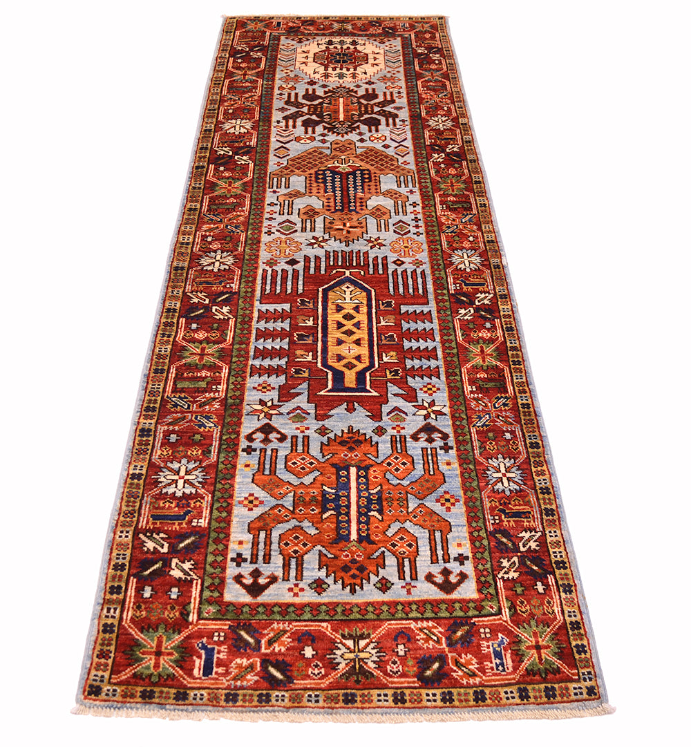 A long rectangular antique looking tribal Afghan runner rug with an intricate geometric and floral pattern, featuring a central field and detailed borders in red, orange, beige, blue, and green, shown flat against a white background.