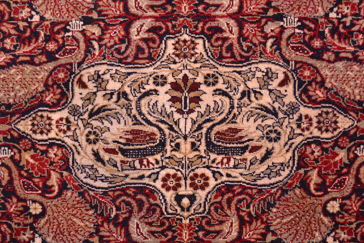 Old Belouch-Tavusi rug close-up of central cream medallion on red patterned background.