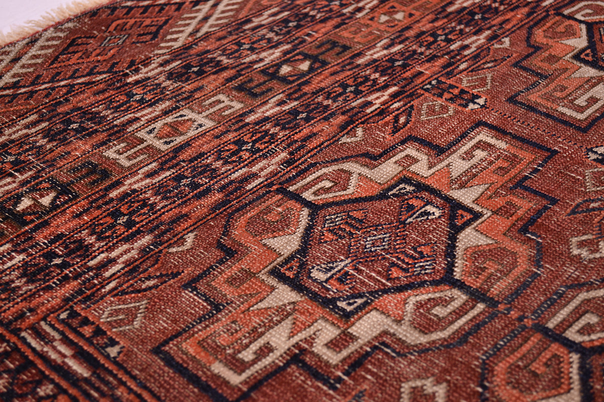 Close-up of a woven antique Turkoman Tekke rug with an intricate geometric pattern in terracotta, orange, beige, and dark brown.