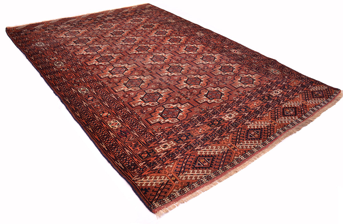 A traditional oriental fine antique Tekke rug with a geometric pattern in shades of red, brown, and beige, shown from an elevated angle on a white background.