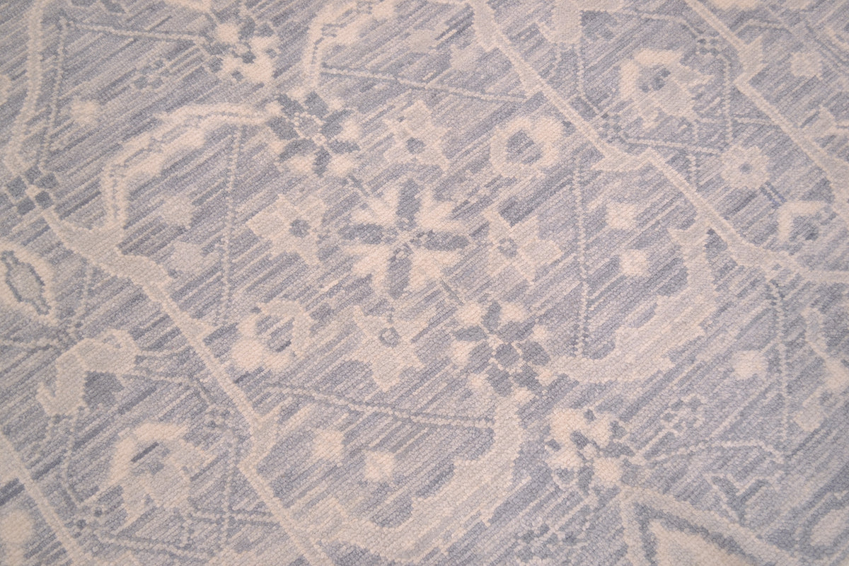 A close-up of a woven textile with a faded floral and geometric pattern in light blue/grey and off-white.