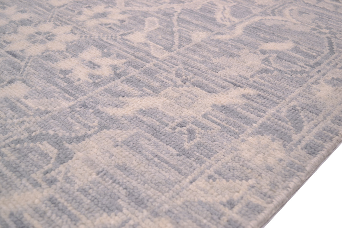 A close-up of a textured area rug with a floral geometric pattern in light gray and cream.
