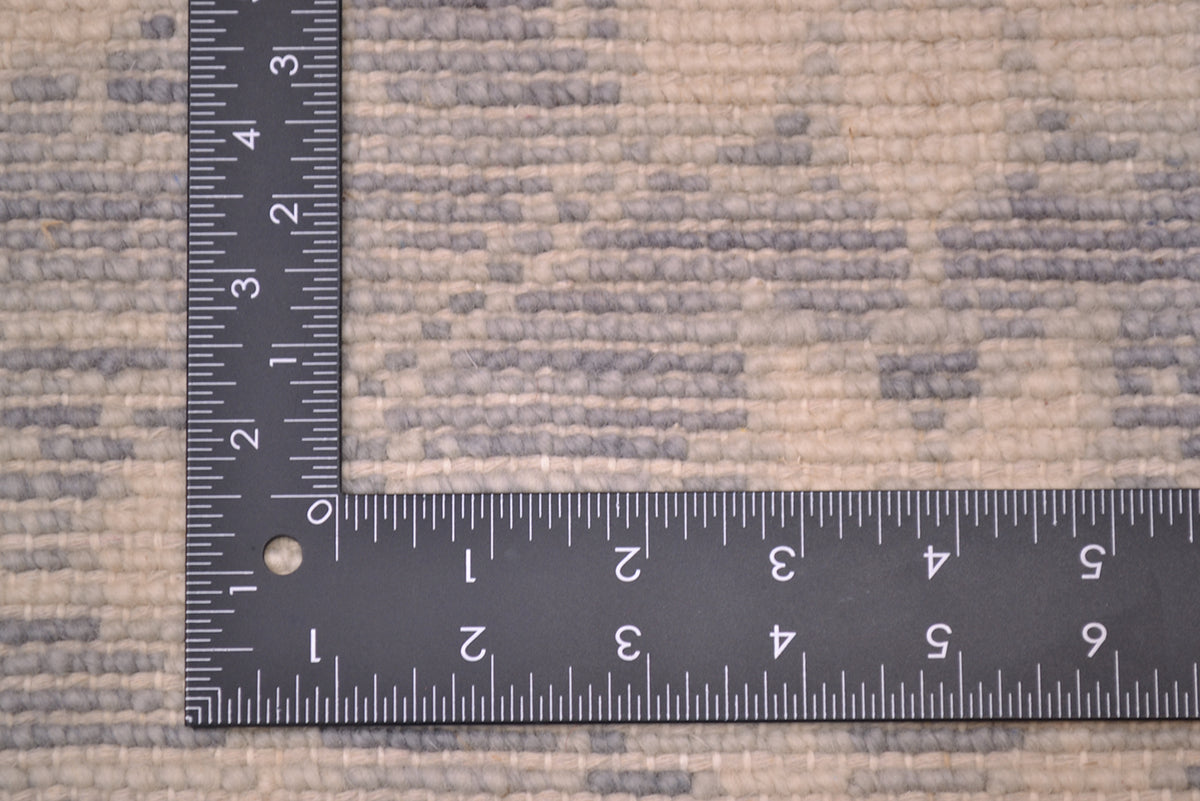 A close-up of a tonal area rug with a black metal ruler on the corner of the rug to indicate to show scale