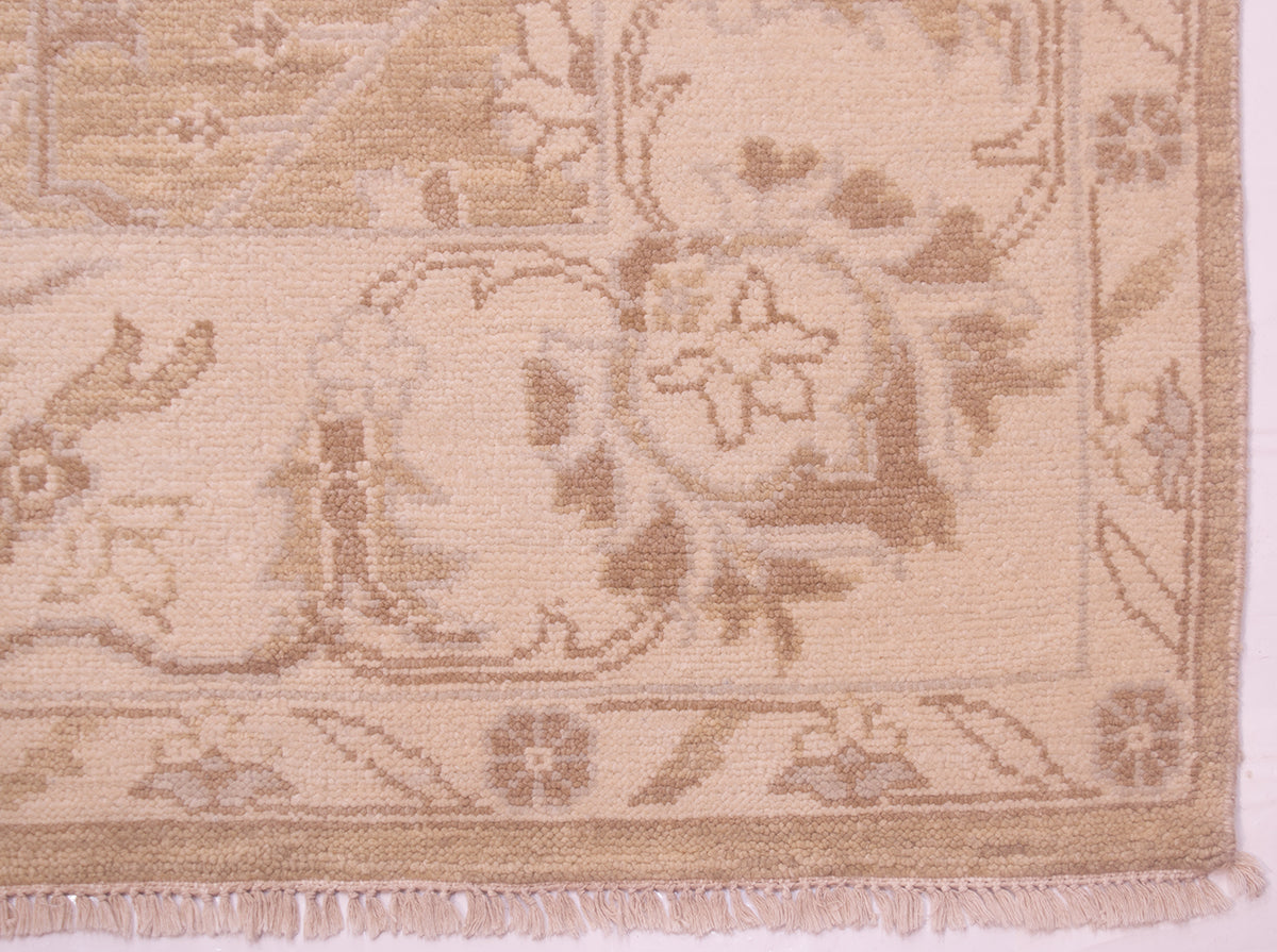Close-up of a beige and tan patterned tonal rug corner with woven floral motifs and short fringe along the edge.