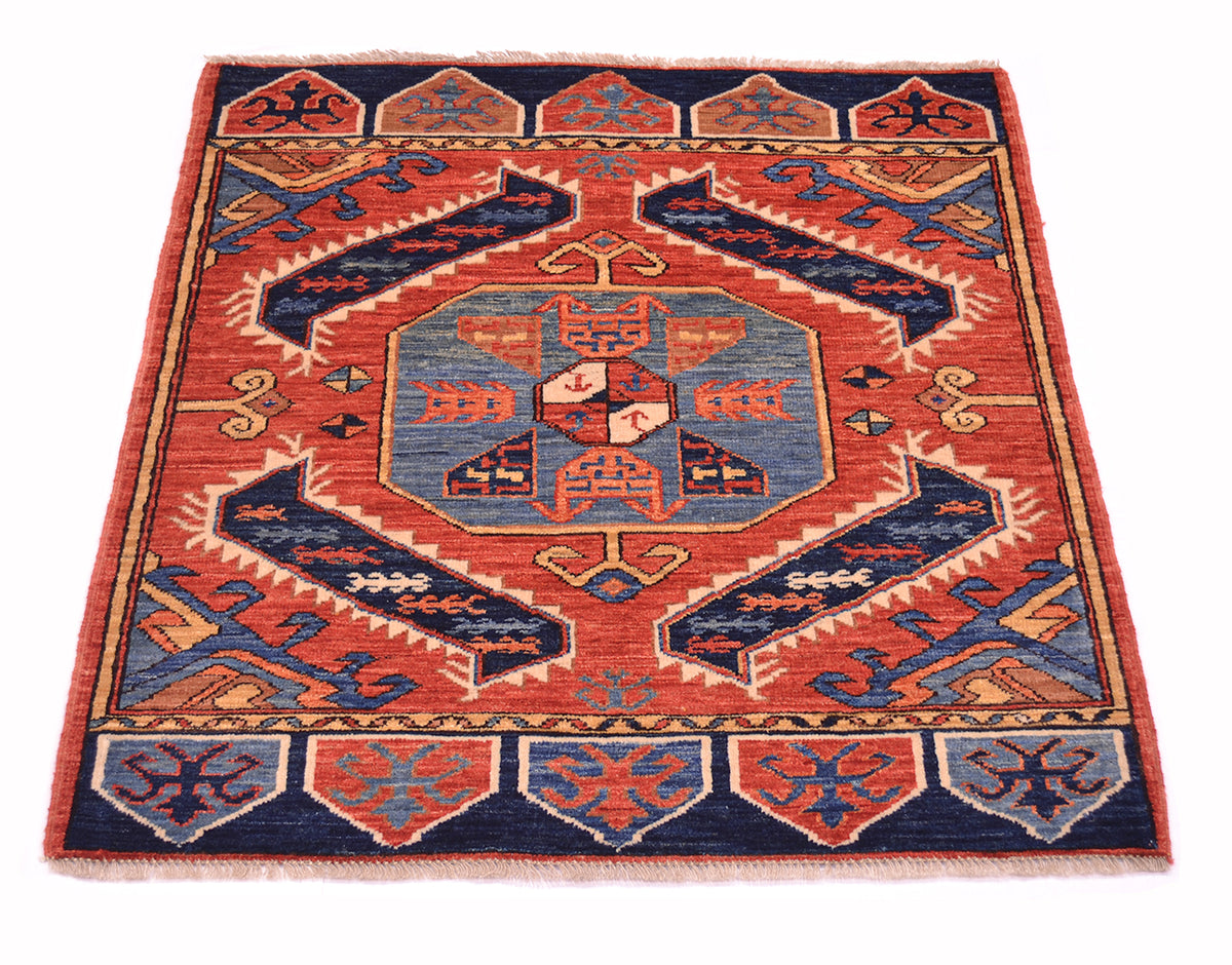 A square hand-woven rug with a traditional geometric pattern in rust red, navy blue, and light blue, displayed flat against a white background.