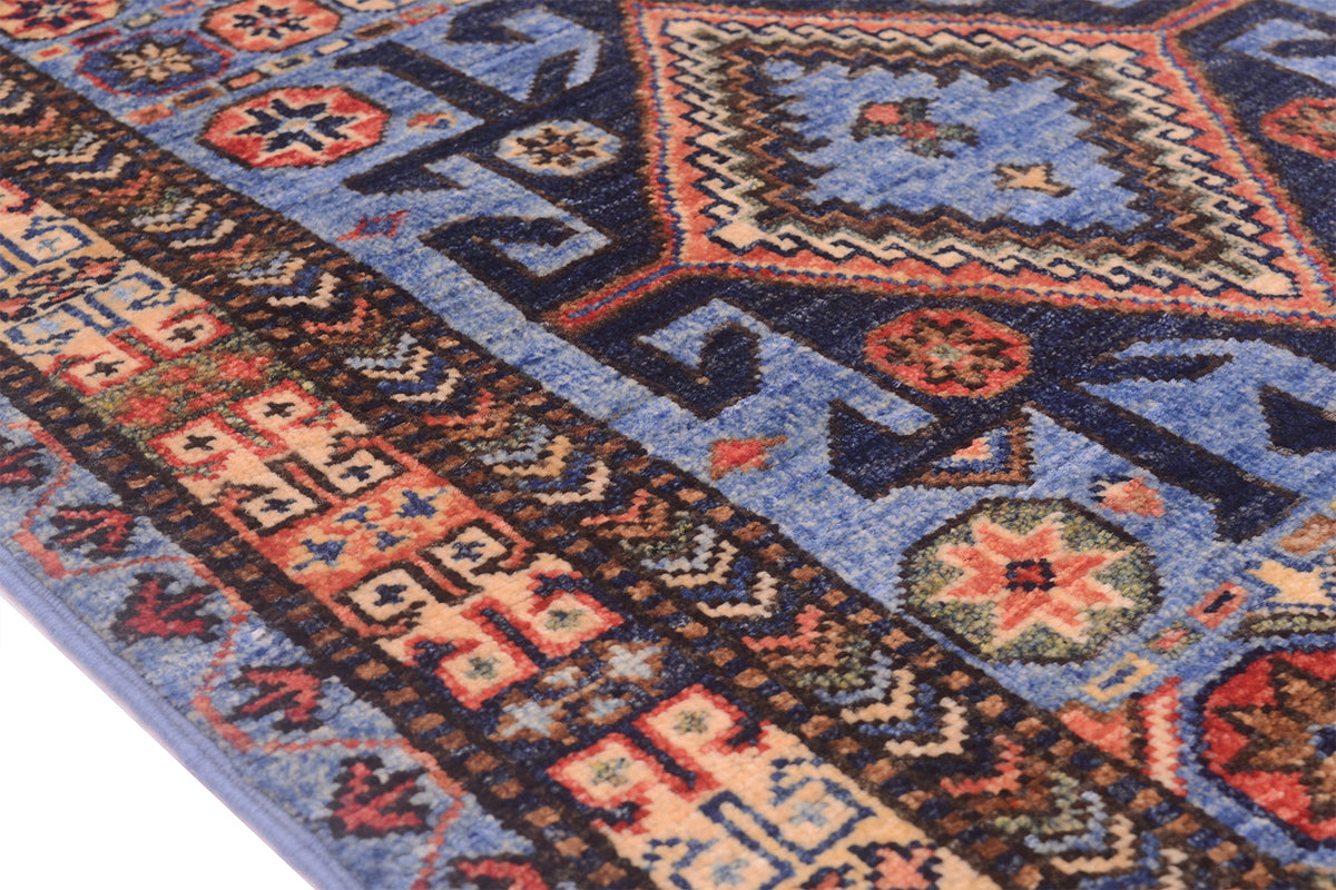 A close-up of a traditional patterned Afghan Turkmen runner with a blue field, dark navy borders, and geometric motifs in red, beige, and green.
