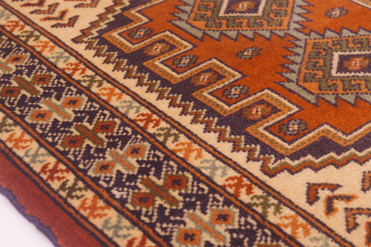 A close-up of a traditional rug mat showing its detailed woven design in orange, beige, brown, and dark blue.