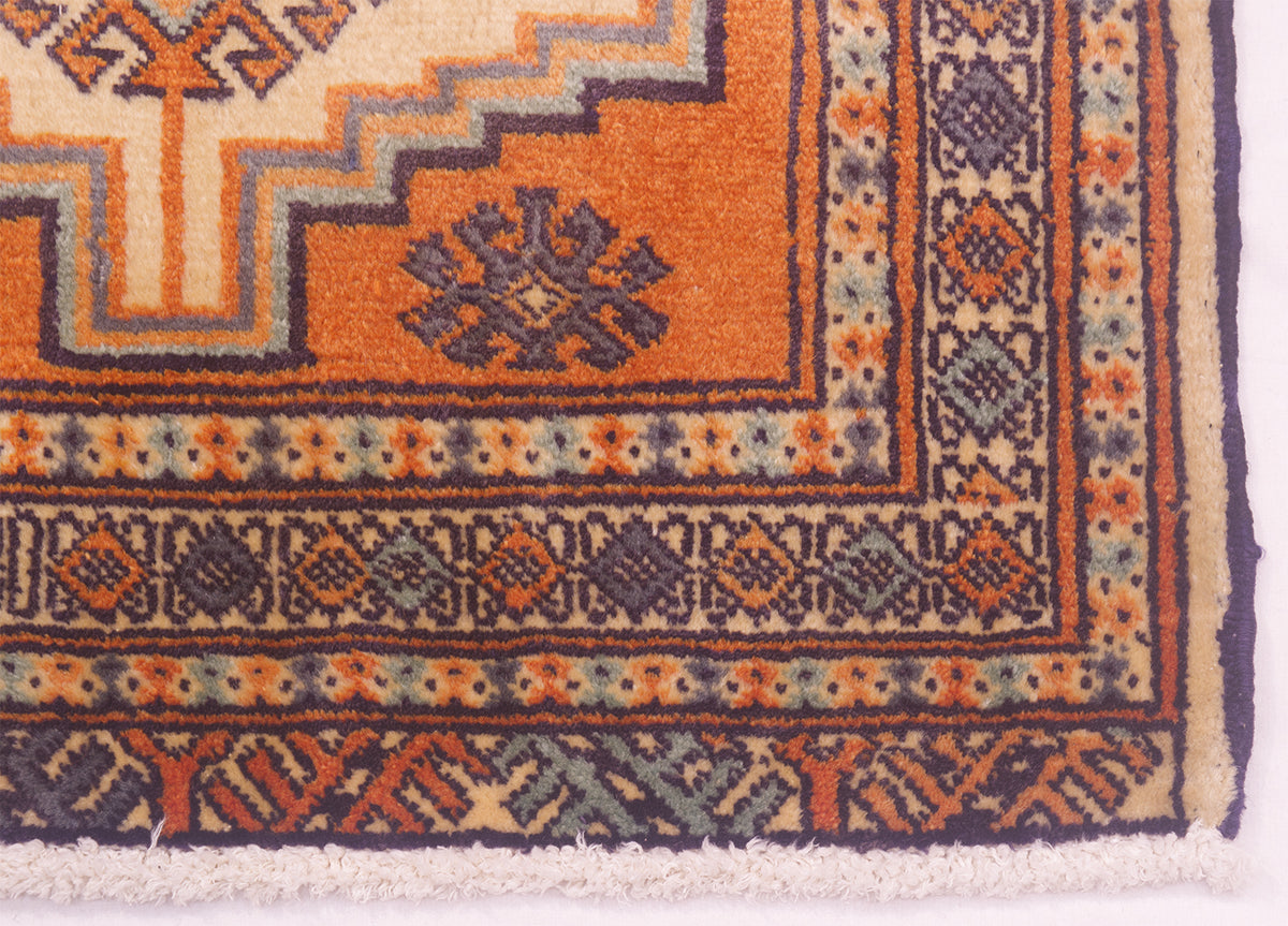 Close-up of corner of a patterned rug showing an orange field with navy, beige, and muted blue geometric borders and motifs.
