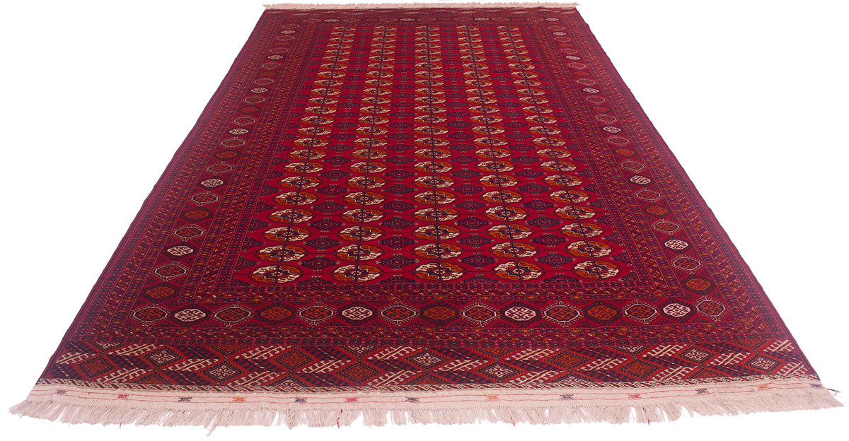 A traditional style Turkoman Bokhara wool rug with a deep red field, intricate geometric and floral motifs in navy, beige, and brown, and cream fringe on the ends.