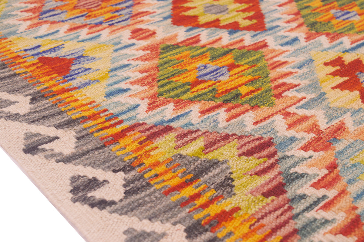 Close-up of a Afghan handwoven Kilim rug with a geometric multicolour pattern in orange, yellow, green, blue, red, cream and grey on a white base.