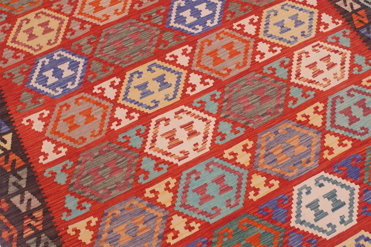 A close-up of a woven kilim rug with a geometric pattern in red, orange, blue, beige, and teal.