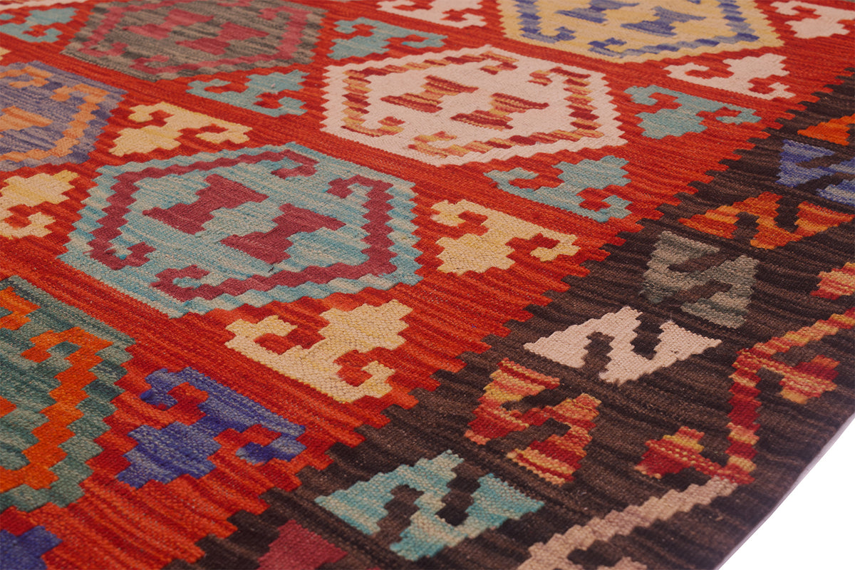 A close-up of a woven kilim rug with a vibrant red-orange base and geometric patterns in brown, beige, light blue, and dark brown.