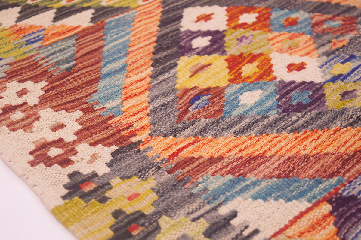 A close-up of a woven kilim rug showing its detailed geometric patterns and multicolor design, featuring orange, blue, yellow, red, and beige tones.