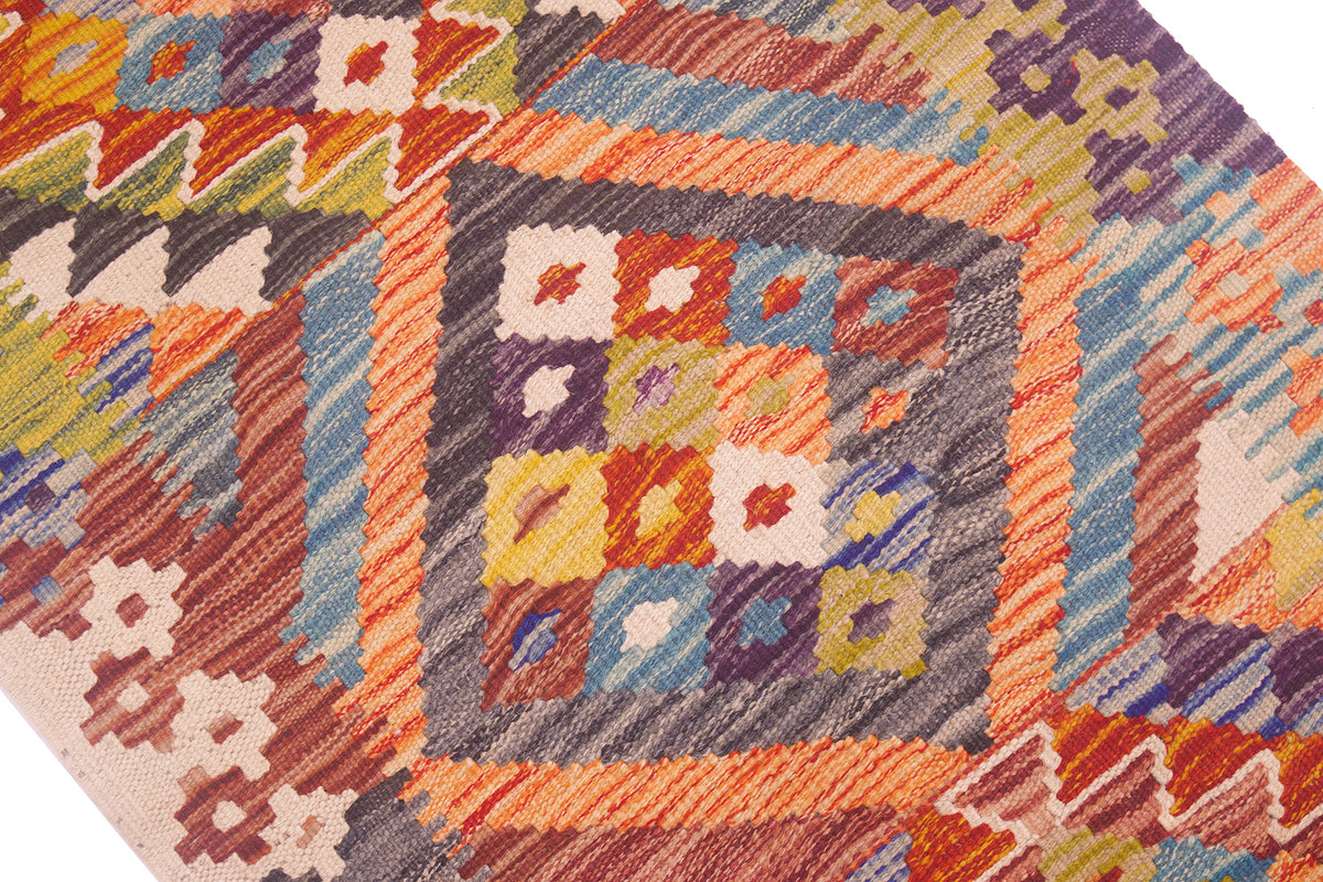 A close-up of a colourful woven kilim strip with a geometric pattern, featuring orange, blue, purple, yellow, and beige tones in a square medallion design.