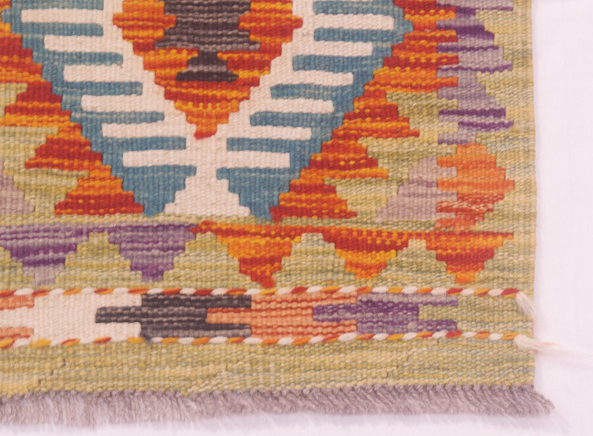 Close-up of a handwoven Afghan Kilim strip corner showing a geometric pattern with orange, blue, purple, beige, and brown threads, finished with a fringed edge.