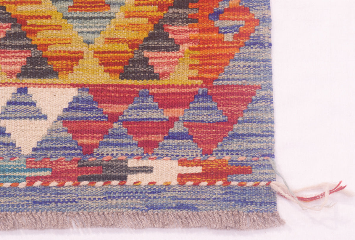 A close-up of a woven kilim strip showing its colourful geometric pattern and fringed edge against a white background.