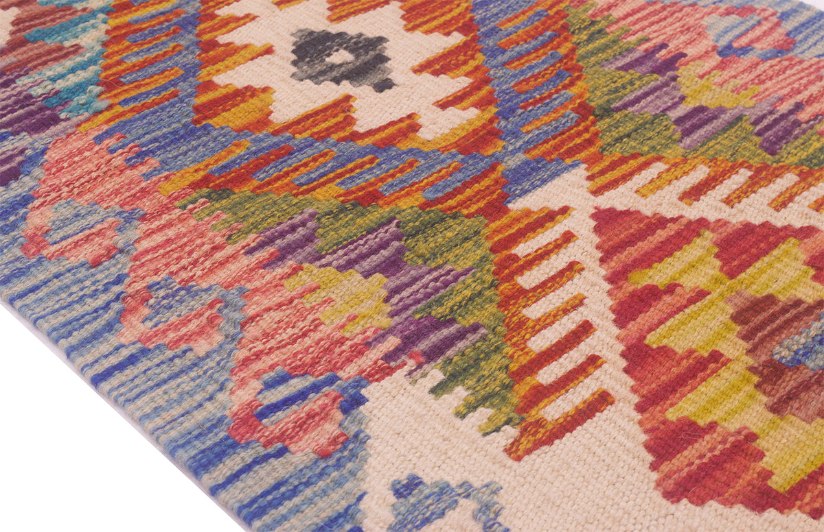 A close-up of a colourful geometric small Kilim strip/runner with a handwoven texture, featuring a cream base with vibrant patterns of red, orange, blue, green, yellow, and purple.