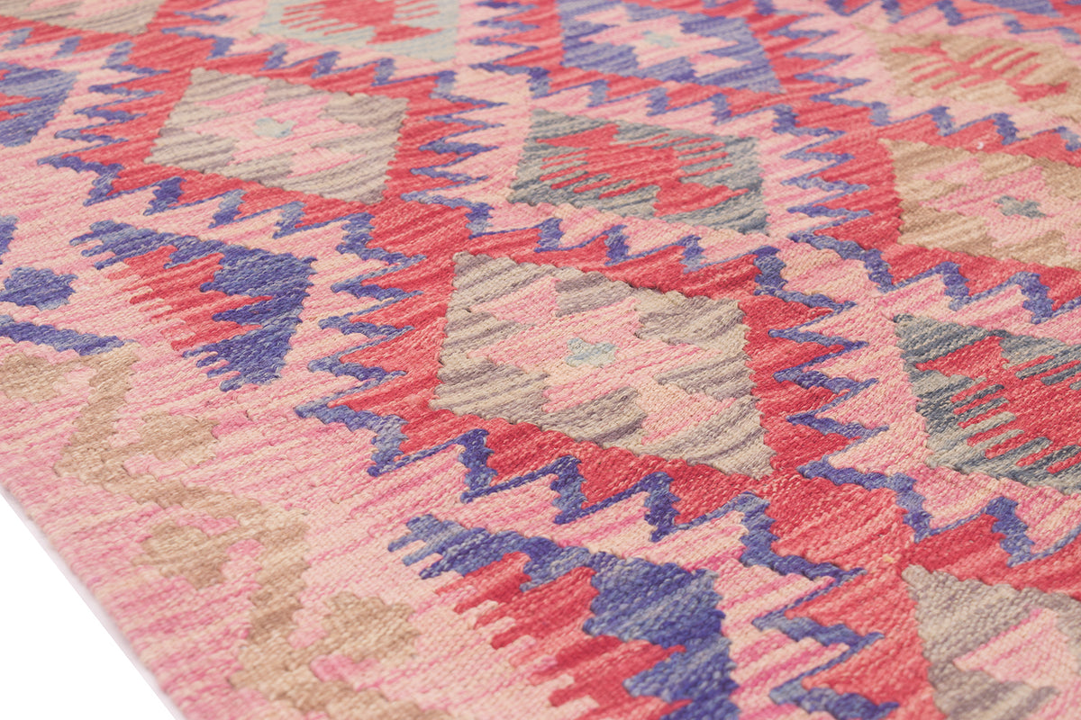 A close-up of a woven Afghan Kilim rug with a geometric pattern in pink, red, blue, beige, and grey.