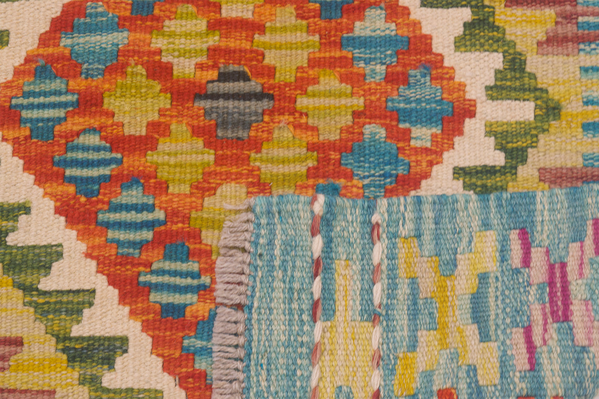 Close-up of a Afghan Kilim Short Runner with a geometric pattern in orange, blue, yellow, green, pink, and cream, showing the texture of the weave and a fringed edge.