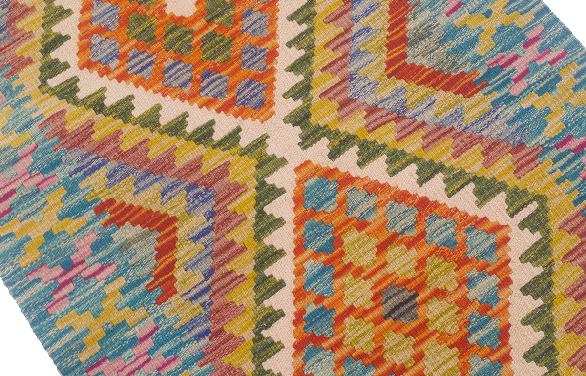 A close-up of a woven kilim runner featuring a vibrant geometric pattern with orange, blue, green, pink, and yellow motifs on a cream background.