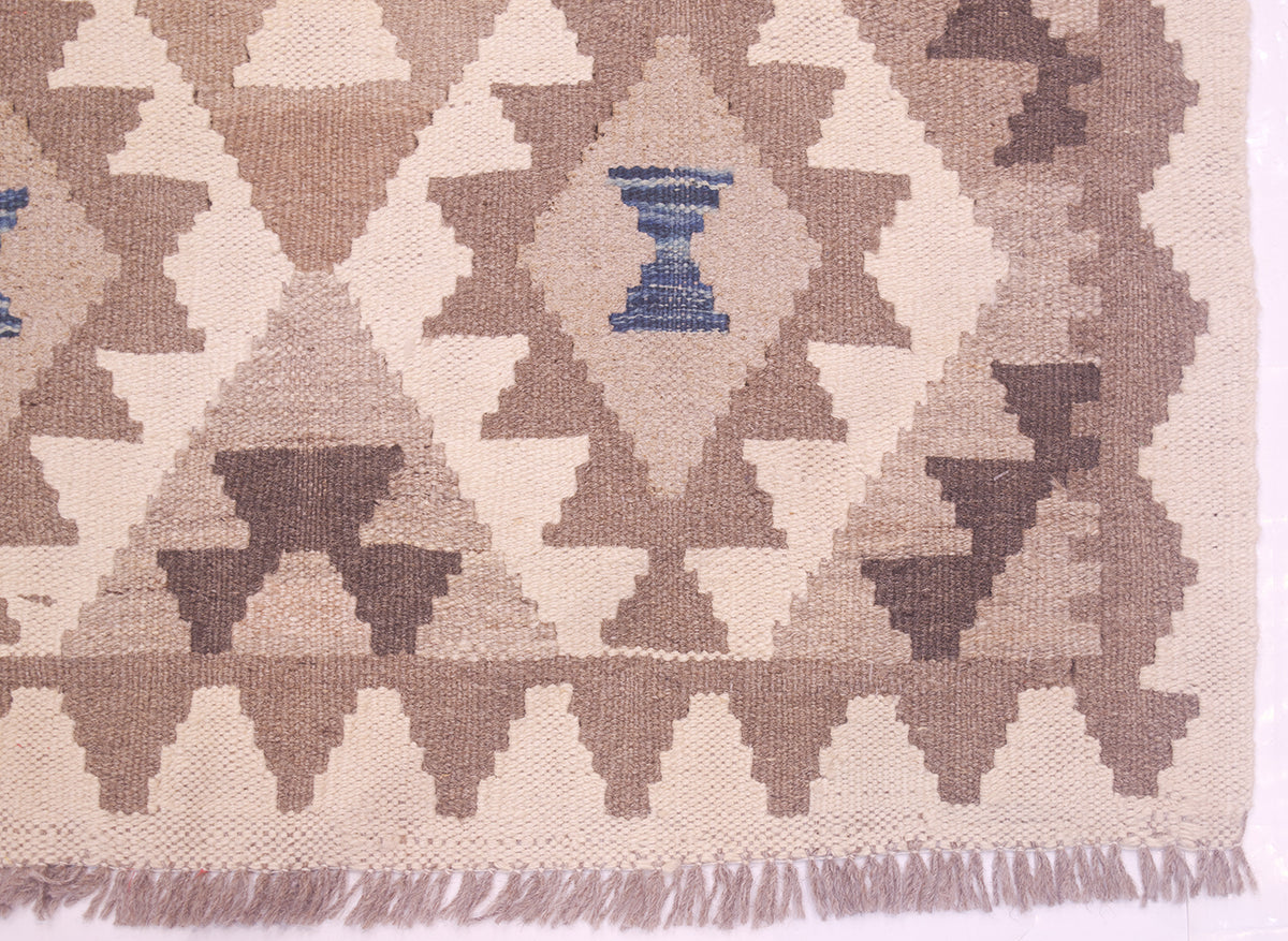 Close-up of a woven Afghan Natural Dye Kilim Runner with a geometric diamond pattern in beige, taupe, brown, and a small blue accent near the top center, with fringe visible along the bottom edge.