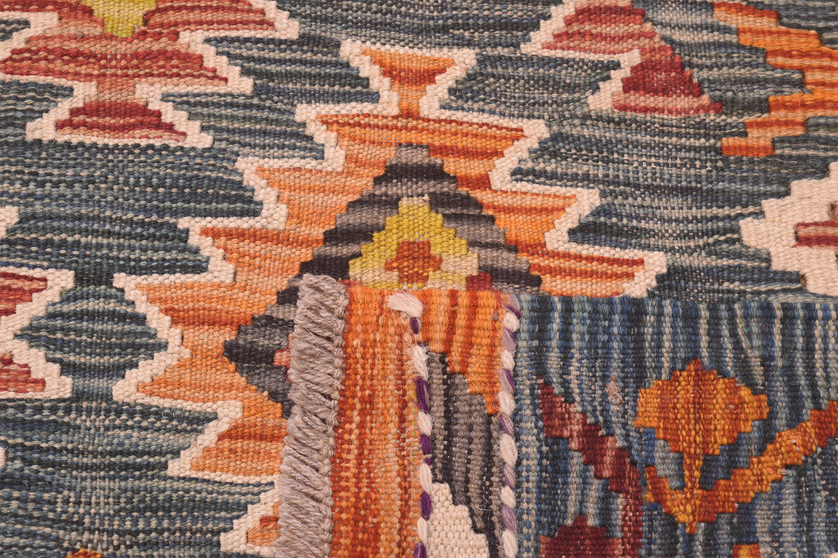 Close-up of a large handwoven kilim rug showing a geometric pattern with orange, dark green, cream, and rust tones.