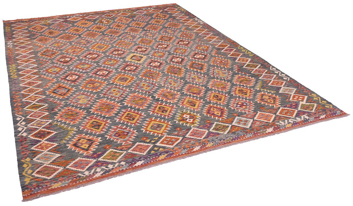 A large kilim area rug with a complex geometric pattern in green, rust red, orange, and cream, shown from an elevated perspective on a white background.