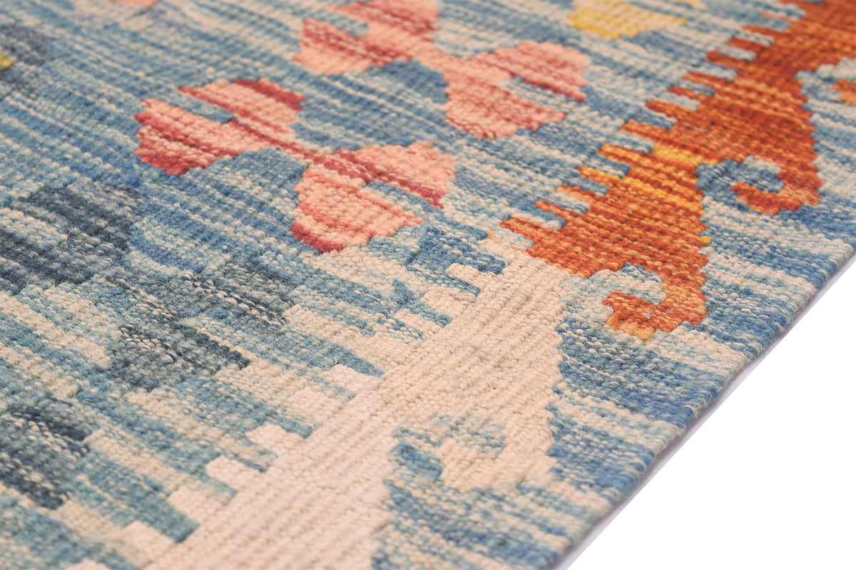 Handwoven kilim rug corner detail with light blue ground and coral diamond motifs