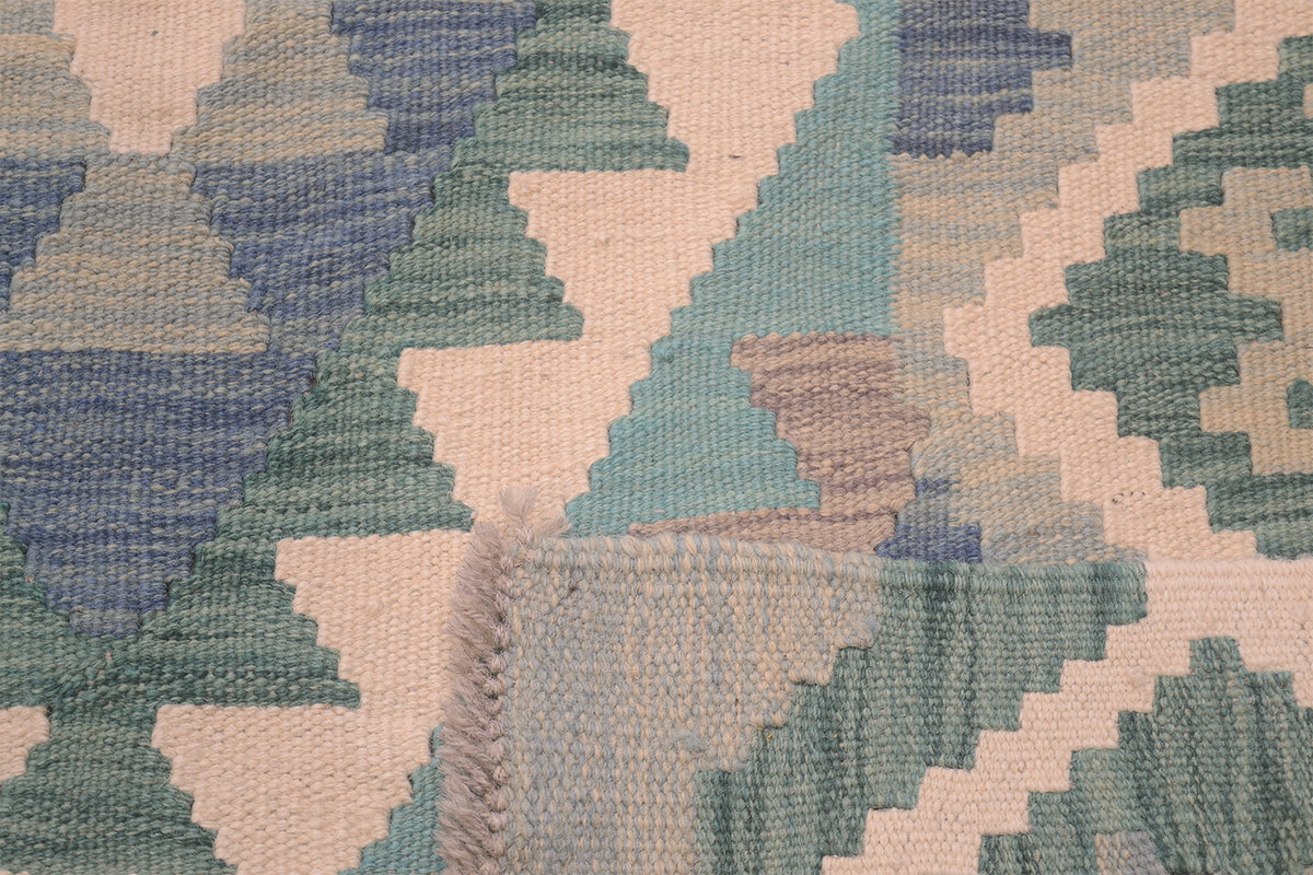 Close-up of a handwoven Afghan Kilim floor rug with a geometric pattern in muted blue, sage green, beige, and light aqua tones.