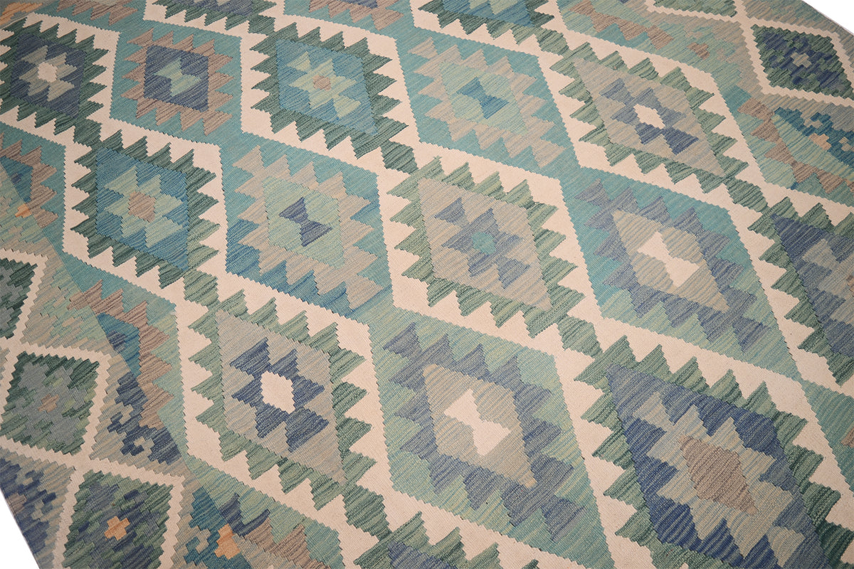 A close-up of a handwoven Afghan Kilim with a repeating geometric diamond pattern in green, teal, blue, beige, and grey tones.