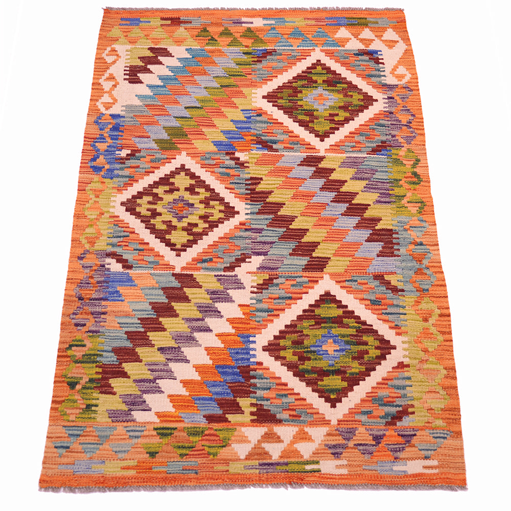A flatweave kilim rug with a vibrant geometric pattern featuring orange, brown, green, blue, and beige diamond motifs on a white background.