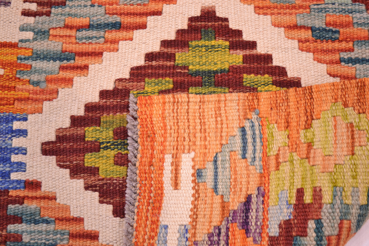 Close-up of a Handwoven Afghan Kilim wool rug showing a geometric pattern in orange, brown, cream, green, blue, and purple.