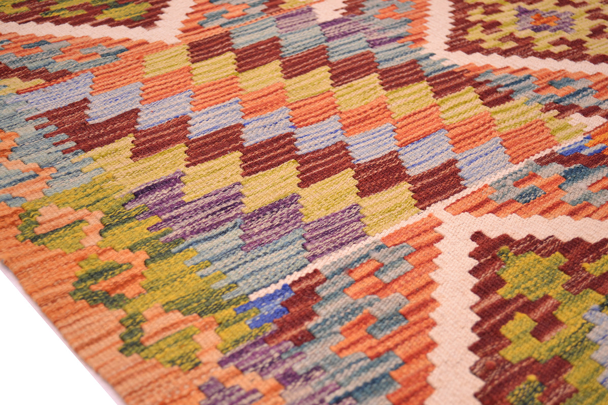 A close-up of a woven kilim rug showing a colorful geometric pattern with orange, yellow, purple, blue, and brown blocks on a cream background.