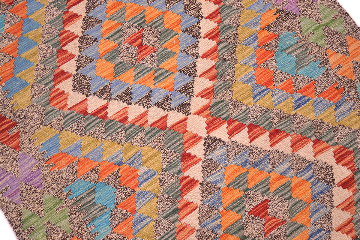 A close-up of a Afghan handwoven Kilim Rug with a multicolour geometric pattern featuring diamond and triangle motifs in orange, blue, red, green, beige, and purple.