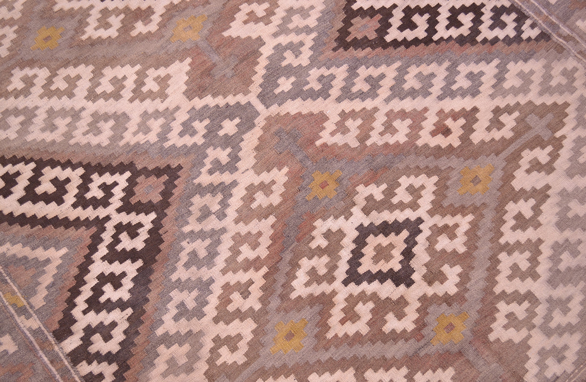 A close-up of a patterned old kilim rug with geometric tribal-style motifs in beige, brown, grey, and muted yellow.