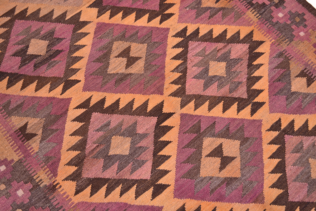 A close-up of a woven old Afghan Kilim wide runner rug with a geometric pattern in dusty pink, mauve, tan, and dark brown.