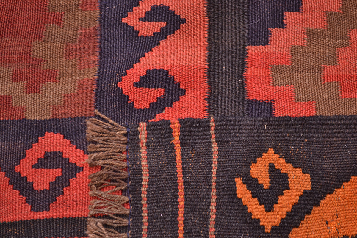 Close-up of a authentic old handwoven Afghan Kilim showing geometric patterns in rust red, orange, and dark navy blue with brown fringe.