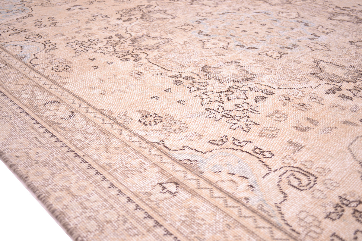 Close up detail of angled edge border of vintage carpet with dark brown fine of floral carpet detailing patterning in soft cream beige and light blue coloured corner sprandrels.