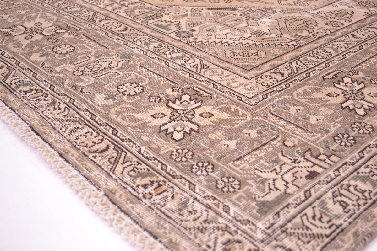 Corern detailng showing shaved zero distressed pile fo vintage carpet in beige, gold and brown. Hints of sage green in detailing but subtle hue. Floral geometirc traditonal format with softened colours. Notice signature of weaver in innerborder.