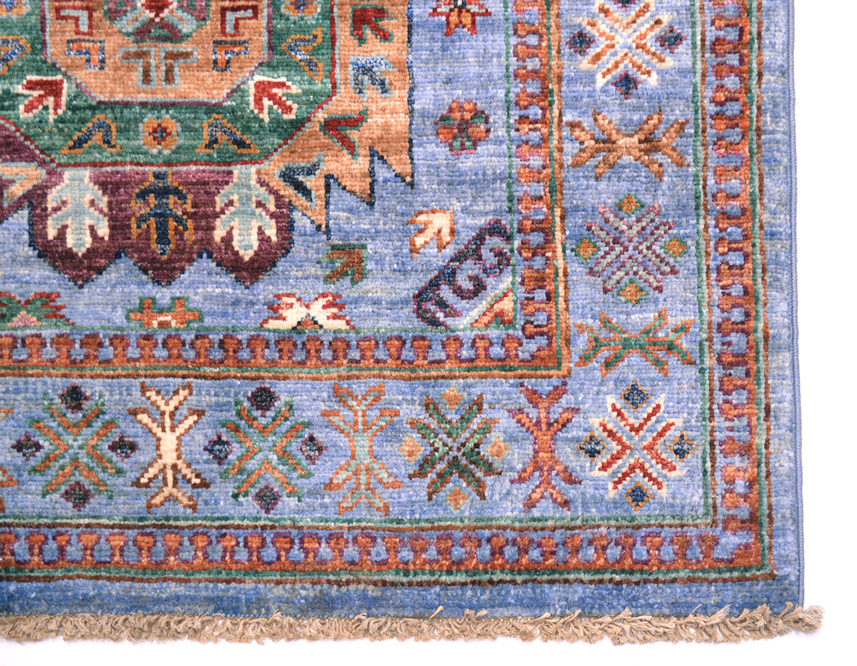 A close-up of a traditional patterned Afghan runner showing the corner and fringe. The runner rug features a blue field with intricate geometric and floral motifs in rust red, beige, green, and brown.