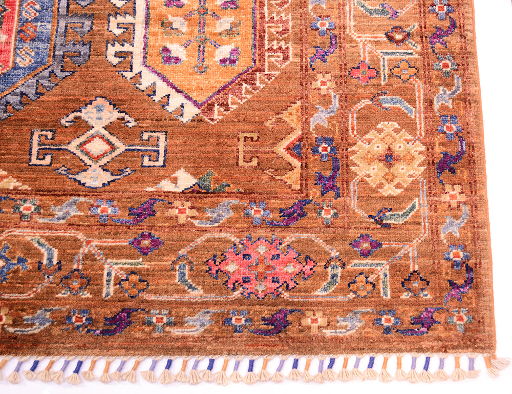A close-up of a traditional handwoven Afghan Waziri rug showing its detailed pattern and texture. The rug features a warm brown base with intricate geometric and floral motifs in orange, purple, blue, and beige.
