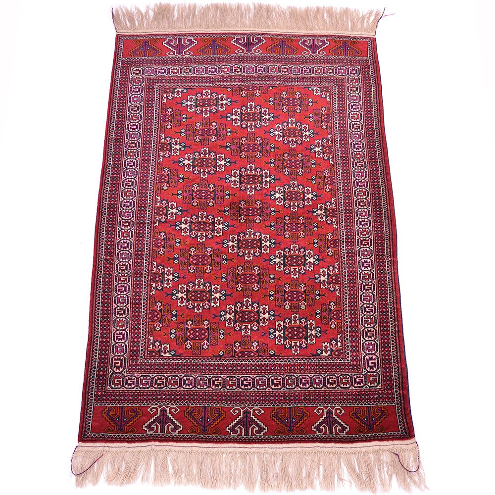 A traditional rectangular hand-knotted Turkoman Yamoud wool rug with a vibrant red field, intricate geometric and floral motifs, and cream-coloured fringe on the top and bottom edges.