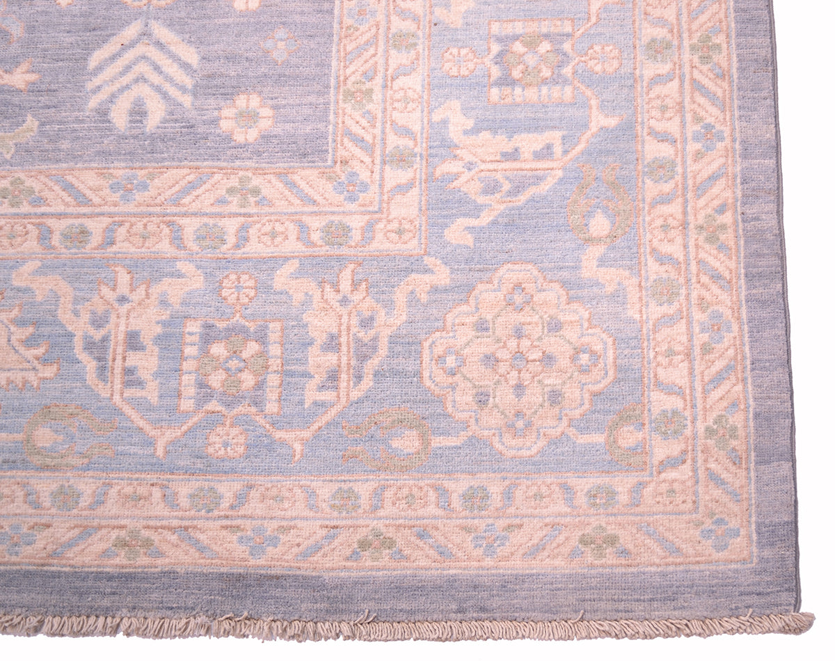 Corner of pastel blue patterned rug with pinkish border trim and fringe